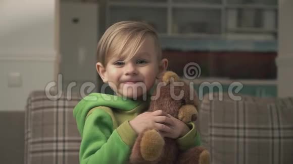 可爱的小男孩穿着绿色睡衣拥抱他的泰迪熊看着相机微笑快乐快乐的孩子视频的预览图