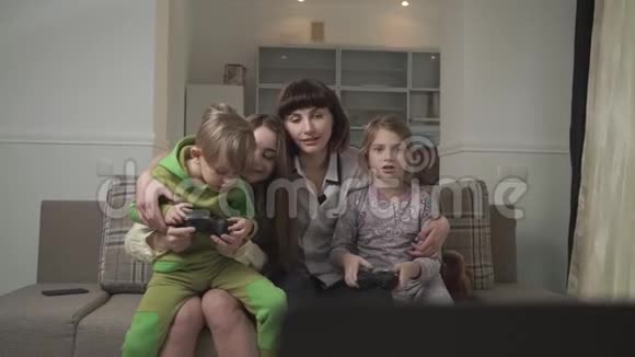 快乐的姐姐和快乐的小朋友坐在沙发上在客房里玩电子游戏欢乐家庭视频的预览图