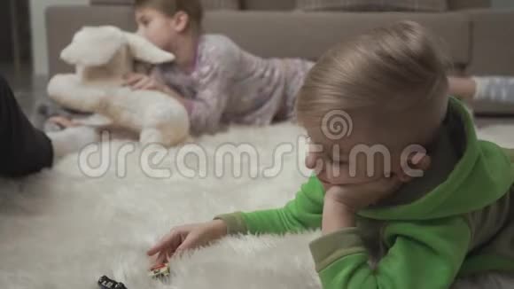 两个可爱的孩子躺在毛茸茸的地毯上玩玩具在地板上孩子们周末快乐视频的预览图