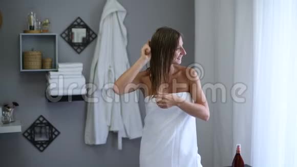 淋浴后裹着毛巾的漂亮女人用木毛刷刷她湿漉漉的头发视频的预览图
