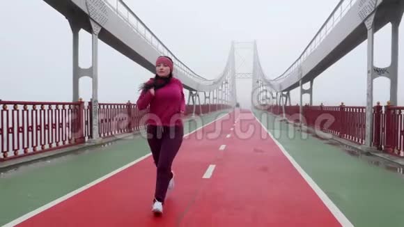 年轻胖乎乎的白种人女孩在桥上奔跑前射慢动作紫色服装视频的预览图
