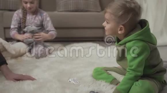 两个可爱的孩子躺在地上毛茸茸的地毯上在家玩玩具男人的手把男孩弄得一团糟视频的预览图