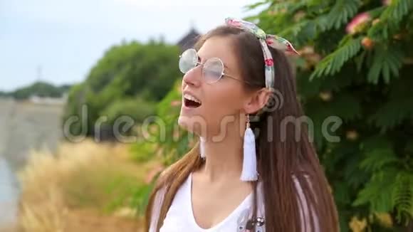在背景树上戴着眼镜头上戴着蝴蝶结的美丽的黑发女孩在欢呼和微笑视频的预览图