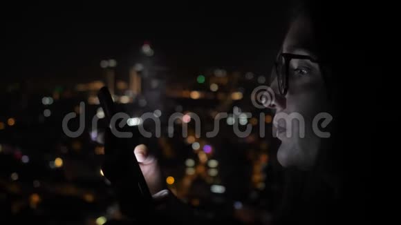 微笑的女人看着窗户附近的智能手机有城市的景色侧面的景色视频的预览图