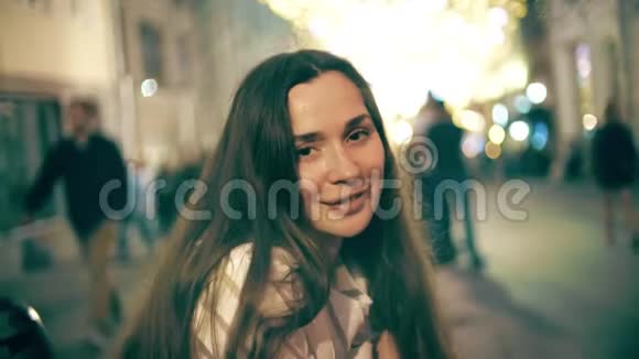 一位笑容满面的年轻女子在照亮的步行街背景下视频的预览图