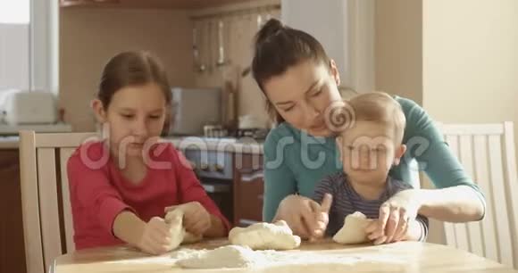 在阳光明媚的日子家庭一起做饭和母亲女儿和儿子一起在厨房里揉面团视频的预览图