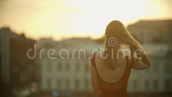 一个穿着红裙子的年轻女子站在屋顶上修头发日落视频的预览图