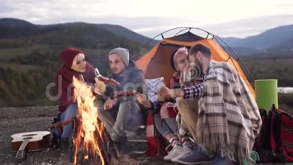 两对可爱的时髦夫妇手里拿着一瓶啤酒在山上的火上煮香肠视频的预览图