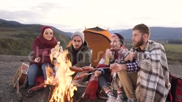 一群快乐的朋友围着一瓶啤酒在山上的火上煮香肠视频的预览图
