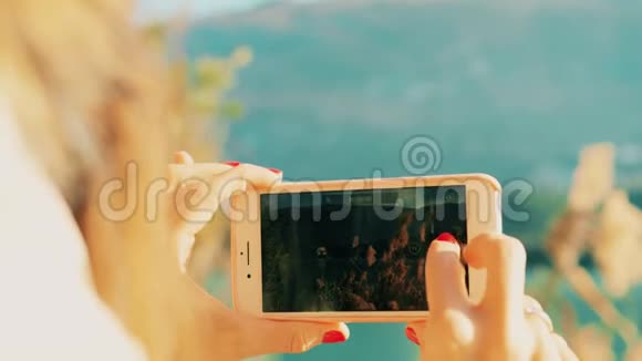 在阳光明媚的一天女人用她的智能手机在湖岸拍摄风景视频红色摄像机拍摄视频的预览图