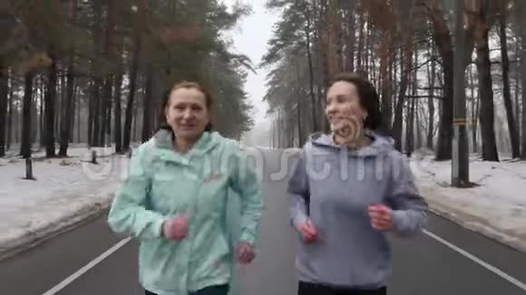 快乐的年长和年轻的高加索女人在冬天的雪地公园里奔跑交谈和微笑关闭前方跟踪射击视频的预览图