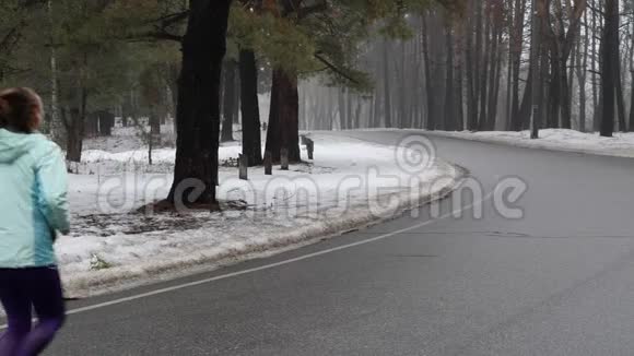 年长的白种人女人戴着耳机在冬天的雪地公园里跑步后退静态镜头慢动作视频的预览图