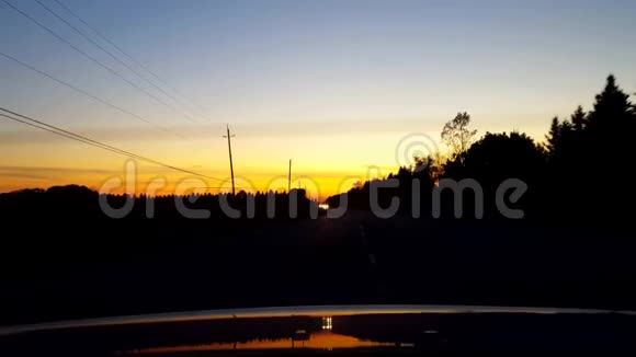 在日落或日出期间从驾驶汽车的乡村道路的背面观看车辆后视角POV视频的预览图