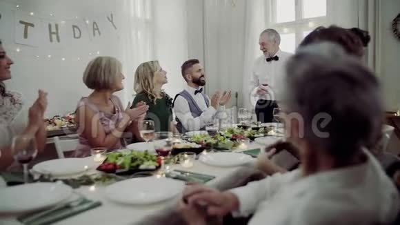 一个大家庭坐在一张桌子旁举行室内生日聚会一位老人发表演讲视频的预览图