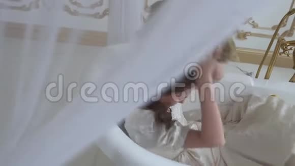 穿着白色婚纱的年轻女子躺在令人惊叹的现代空浴中睡在枕头上视频的预览图