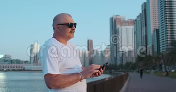 大胡子老人站在户外使用智能手机退休男性通过手机与孩子聊天视频的预览图