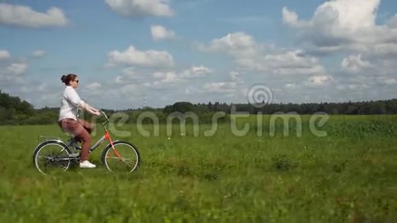 女孩骑着红色自行车穿过绿色的田野视频的预览图