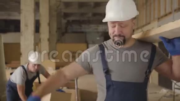 戴白色防护头盔的成年白人男子用木板在施工现场行走的肖像建设者视频的预览图