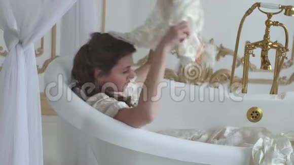 穿着白色婚纱的年轻女子躺在令人惊叹的空浴室里女孩摘下她的帽子戴上鲜花扔进去视频的预览图