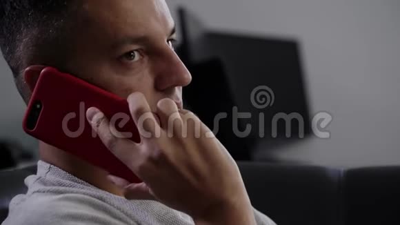一位身穿灰色t恤的黑发男子在沙发上的智能手机上讲话视频的预览图