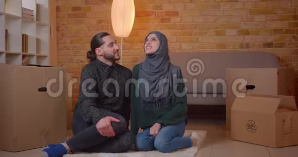一对年轻开朗的穆斯林夫妇坐在新买公寓盒子旁边的地板上微笑着特写镜头视频的预览图