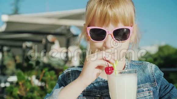 戴粉红眼镜的搞笑女孩在咖啡馆的夏日露台上喝鸡尾酒与孩子们一起休息的概念视频的预览图