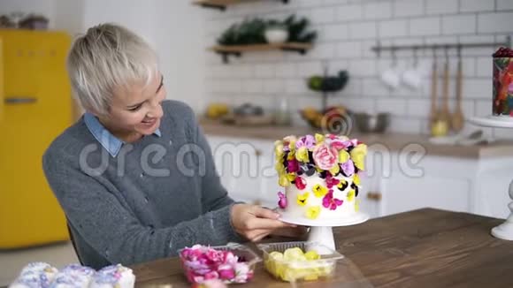 留着短灰头发的女人在白色现代厨房装饰着五颜六色的小白蛋糕视频的预览图