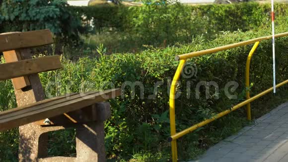 盲人用白色拐杖触摸栅栏找长凳在夏季公园休息视频的预览图