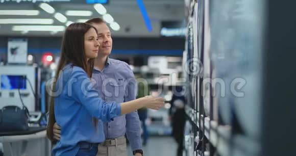 一个英俊的男人和一个女人选择一台洗衣机来买开门检查滚筒和滚筒的涂层视频的预览图
