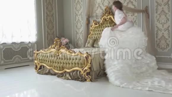 年轻的笑着穿着白色老式球服的漂亮女人跑着跳着来到巨大的金色床前视频的预览图