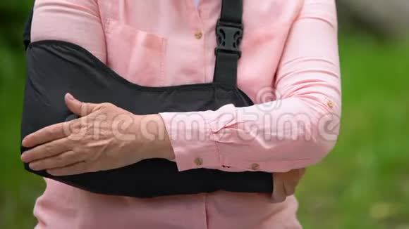 老年妇女用吊带按摩疼痛的手臂站在户外公园外伤视频的预览图