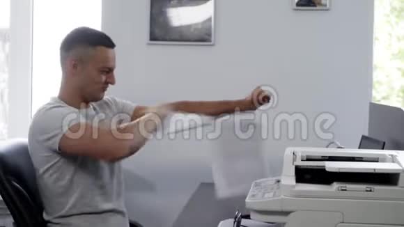 身穿白色t恤面带笑容的英俊黑发男子在办公室撕纸张视频的预览图