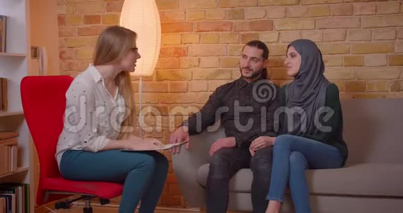 一对年轻快乐的穆斯林夫妇和一个现实的人讨论一间新公寓时他们兴高采烈地坐在公寓上视频的预览图