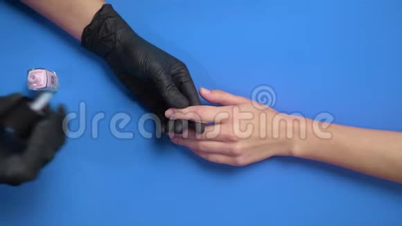 穿黑色橡胶手套的美甲师用透明保护指甲油在背景上涂上指甲油视频的预览图