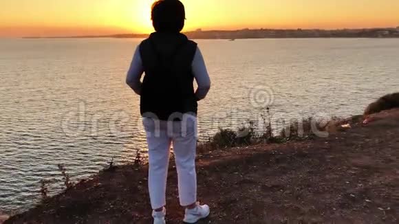 日落时女人高高地站在海面上视频的预览图