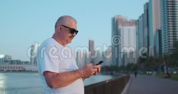 大胡子老人站在户外使用智能手机退休男性通过手机与孩子聊天视频的预览图