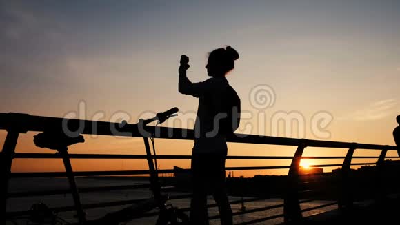一个女孩的剪影为夏天到大海的桥上的日落拍照视频的预览图