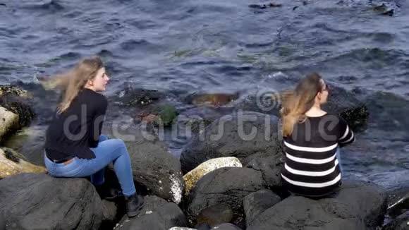 两个女孩坐在北爱尔兰铜锣湾的岩石上视频的预览图