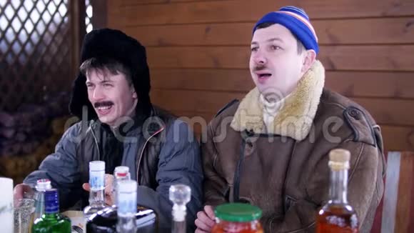 在村里两个男人的朋友围坐在满是食物的桌子旁喝伏特加视频的预览图