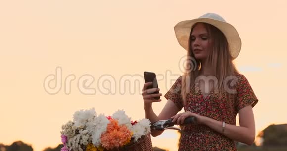 一个漂亮可爱的女孩在阳光明媚的日子里在公园里在自行车旁边用智能手机和手掌一个漂亮的女孩视频的预览图