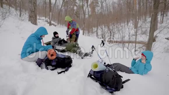 4个人在冬天在森林里徒步旅行躺在雪地里检查背包视频的预览图