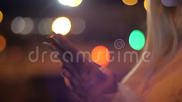 晚上在城市里用智能手机特写金发女人的手在城市街道的智能手机上输入信息视频的预览图