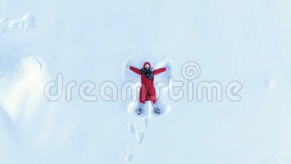空中镜头升起一个穿着红色绒毛的女孩躺着做一个雪天使视频的预览图