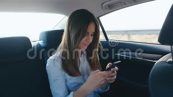 肖像年轻女子在与司机一起乘坐汽车时使用智能手机女孩正在检查指甲聊天视频的预览图