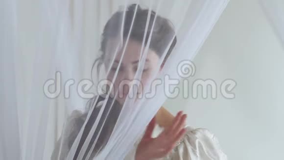 肖像年轻可爱的女人打开薄纱害羞地闭上她的脸白色的羽毛扇在白色的背景上半张脸视频的预览图
