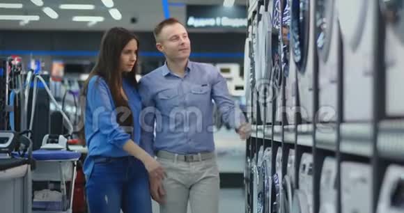 一个英俊的男人和一个女人选择一台洗衣机来买开门检查滚筒和滚筒的涂层视频的预览图