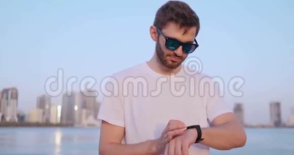 夏天一个站在海滨的年轻人使用智能手表屏幕视频的预览图