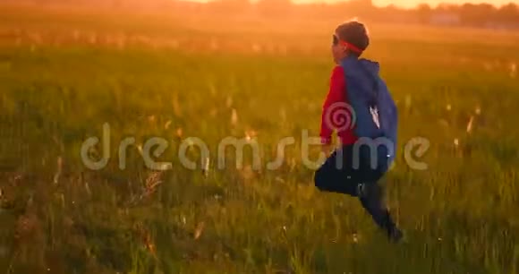 一个穿西装的男孩和一个超级英雄面具在草地上日落时跑过田野视频的预览图
