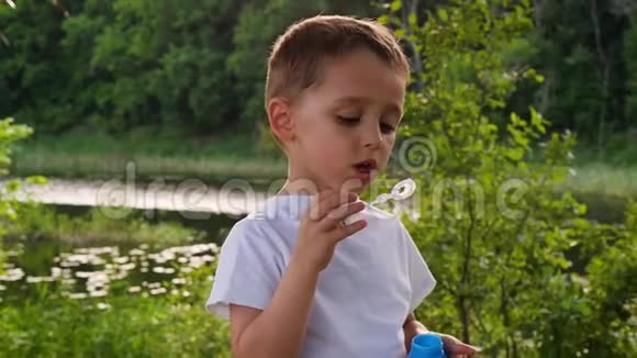可爱的小男孩在湖边的一个绿色公园里充气肥皂泡娱乐和游戏视频的预览图