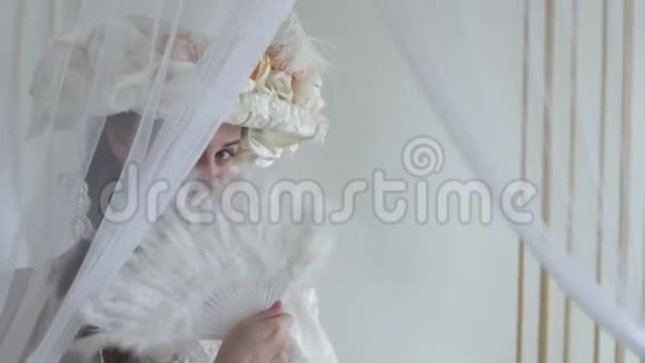 完美的年轻女子戴着丝质帽子戴着花扇脸上挂着白色的羽毛扇躲在面纱后面实际视频的预览图